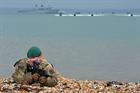 A Royal Marine Commando recces a stretch of beach whilst offshore raiding craft (ORCs) and Landing C